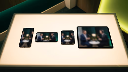 Table lumineuse où trois smartphones et une tablette montrent, flou, le même entretien filmé, sous des lumières vertes