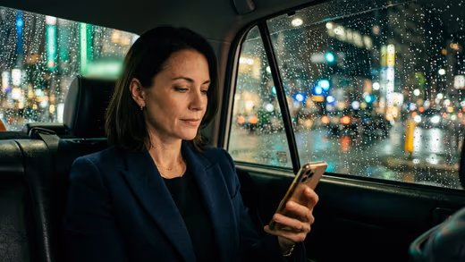 Dirigeante en blazer marine lisant son smartphone à l'arrière d'un taxi, la nuit, vitre mouillée aux reflets verts